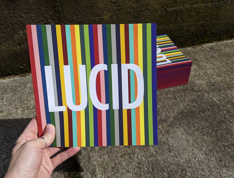 Lucid catalogue cover design featuring multicolour vertical stripes and the show title lucid in large white type.
